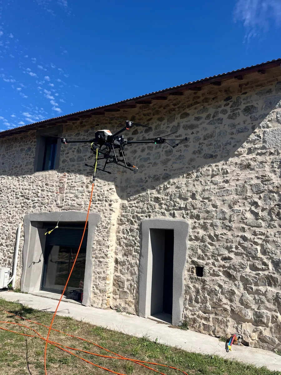 Drone pulvérisant un produit sur une façade en pierre à Annonay